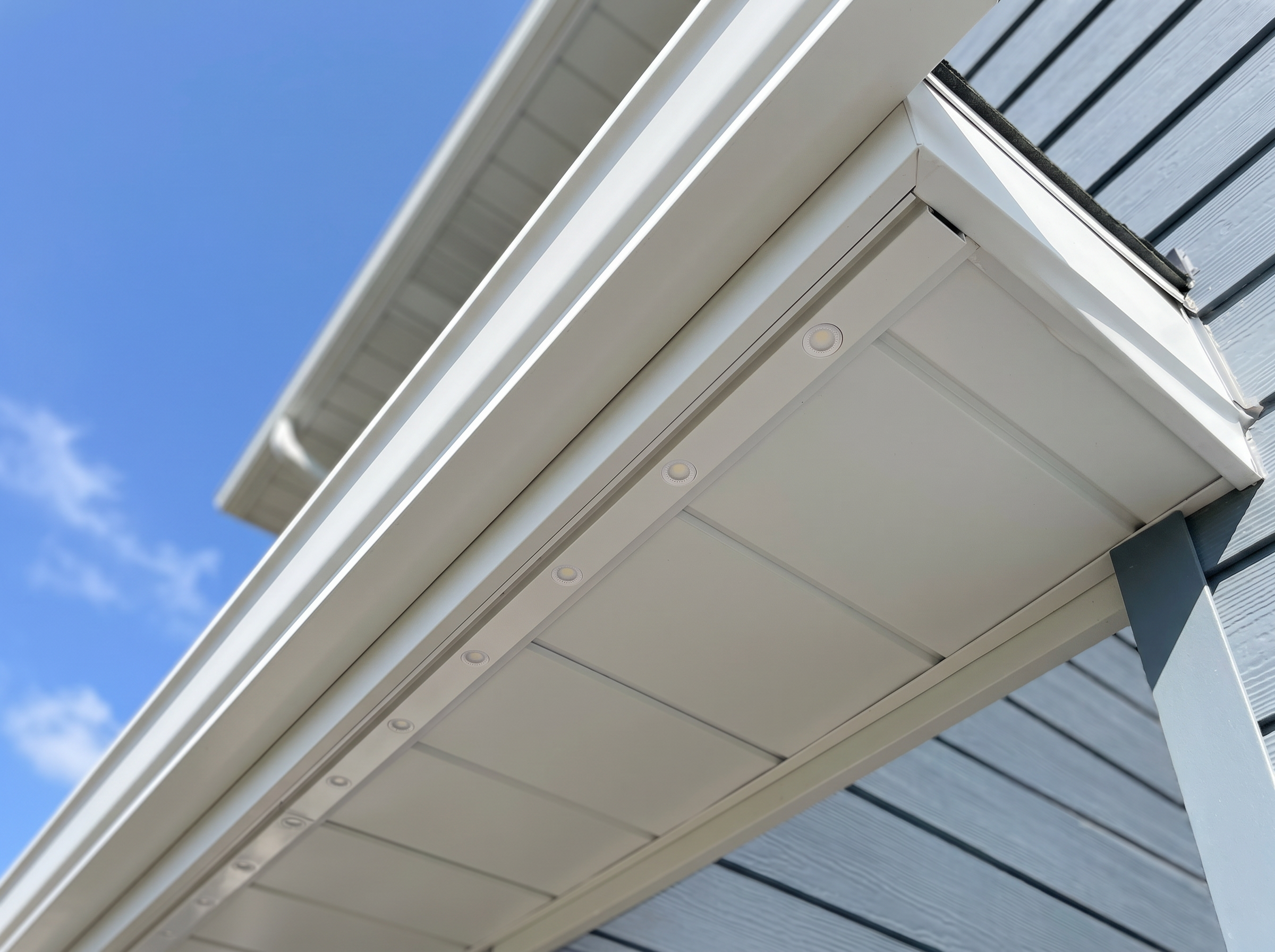 Close-up of slim color-matched aluminum track holding LED point lights, integrated seamlessly into the white soffit of a modern home